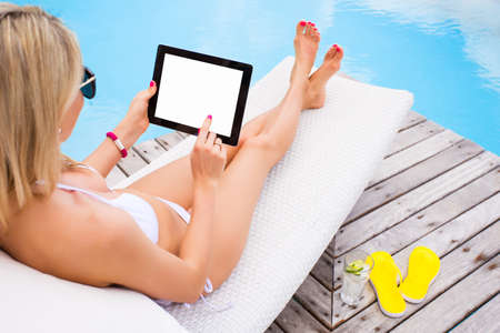 Woman using tablet computer while sunbathing in chair by the poolの写真素材