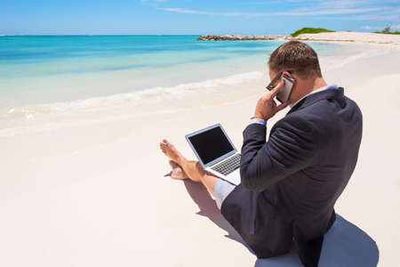 Businessman working with computer and talking on phone on the beachの写真素材
