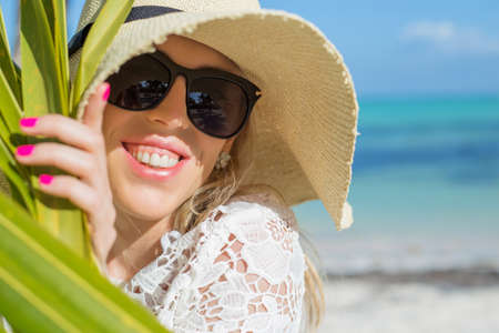 Cheerful woman behind palm leaf on the beachの写真素材