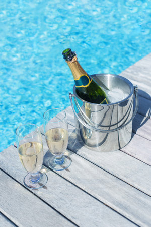 Vertical photo of champagne bottle in bucket and two glasses of champagne on the deck by the...