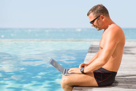 Man using computer by the poolの写真素材