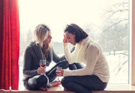 Two female friends talking while sitting at homeの写真素材