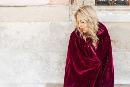 Woman in red cloak sitting on benchの写真素材