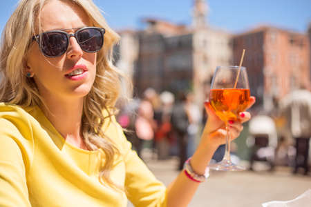 Woman sitting in outdoor cafe and drinking Aperol Spritz cocktailの写真素材