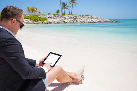 Businessman using tablet computer on the beachの写真素材