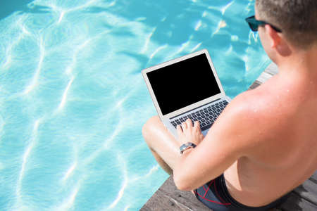 Man with computer sitting by the poolの写真素材