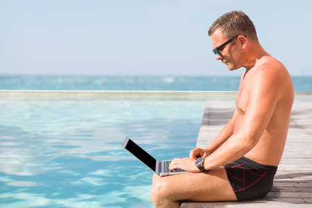 Young man using laptop computer by the poolの写真素材