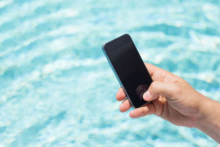 Mobile phone in hand by the poolの写真素材