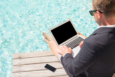 Business man sitting by the pool and working with laptop computerの写真素材