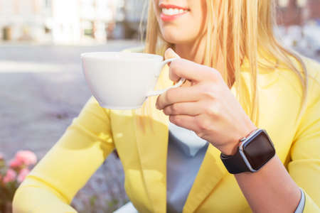 Woman with a smartwatch around her wrist holding a cup of coffeeの写真素材