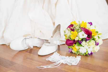 Brides wedding shoes, garter, and flowers sitting on the floorの写真素材