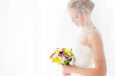 Bride hiding behind veil and looking at flowersの写真素材