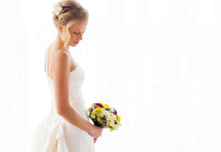 Bride standing by the window in her wedding dress and bouquetの写真素材