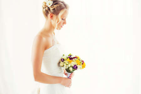 Bride standing by the window with flowers in her handの写真素材