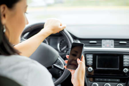 Woman driving and looking at cellphoneの写真素材