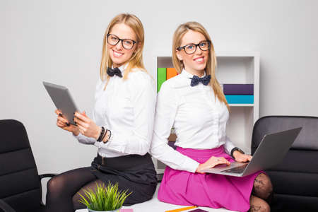Two co-workers sitting on table and holding modern technologyの写真素材
