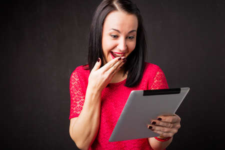 Woman looking at tablet and covering her mouth in surpriseの写真素材