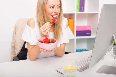 Woman working at the office and eating strawberriesの写真素材