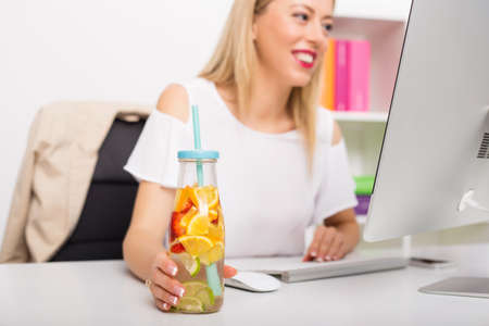 Woman at the office having re-freshening drink while workingの写真素材