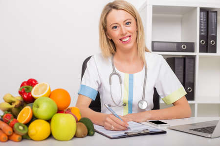 Health doctor in her office with vegetables and fruitsの写真素材