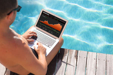 Investor looking at stock quotes on laptop by the poolの写真素材