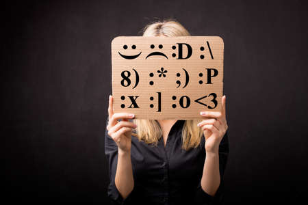 Woman holding cardboard with different emotion smileys in front of her faceの写真素材