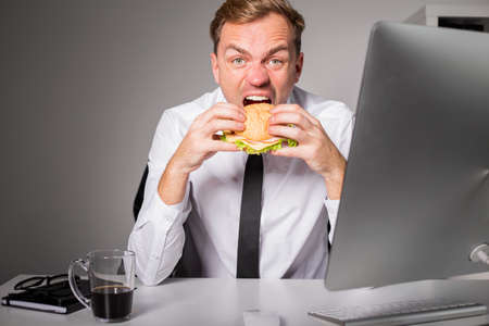 Hungry man at the office eating burgerの写真素材