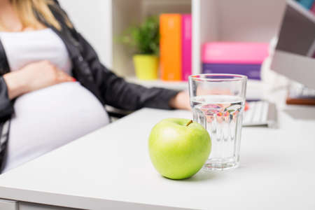 Pregnant woman in office with apple and water glassの写真素材