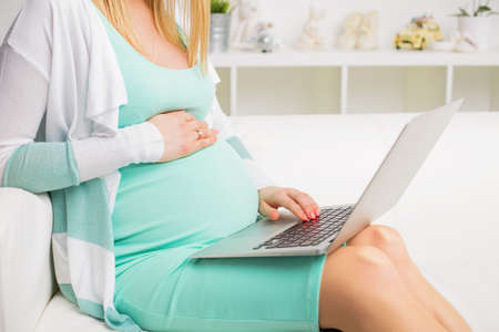 Pregnant woman sitting on couch and using laptopの写真素材