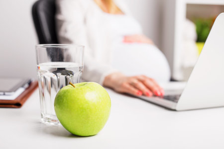 Pregnant woman in office having apple and water