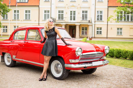 Glamorous woman standing next to red vintage carの写真素材