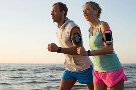 Couple running on the beach during sunset with their headphones plugged inの写真素材