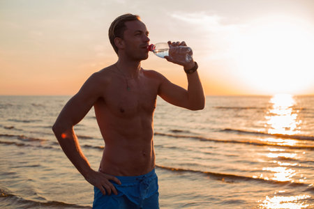 Fit man drinking water by the beach after workoutの写真素材