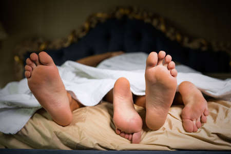 Couple feet hanging out of sheetsの写真素材
