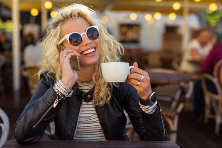 Woman sitting with sun glasses and talking on the phoneの写真素材