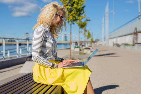Modern woman sitting on the bench outside and working on computerの写真素材