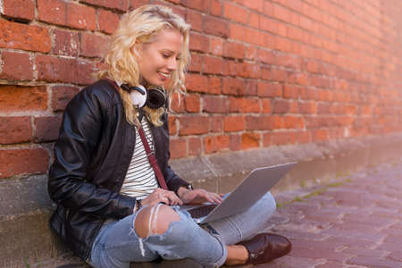 Hipster sitting on the ground in the city and working on computerの写真素材