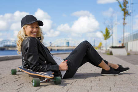 Happy woman with longboard sitting on the groundの写真素材