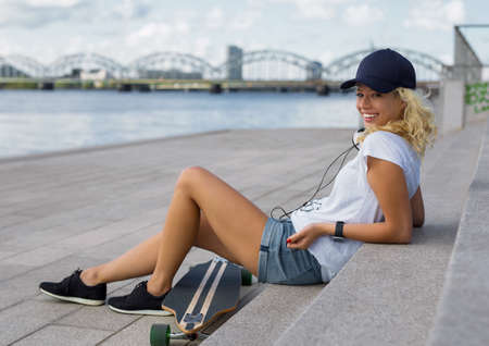 Modern girl sitting on stairs with longboardの写真素材