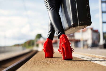 Female with red high heels and suitcase in train stationの写真素材