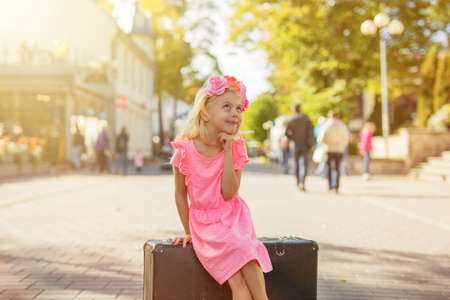 little girl sitting on suitcase and thinkingの写真素材