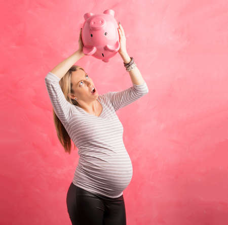 Pregnant woman in shock shaking piggy bankの写真素材