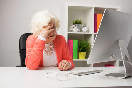 Older woman at the office having headacheの写真素材