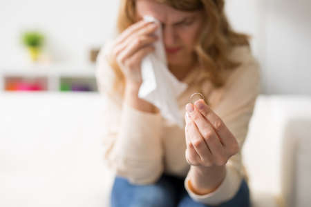 Woman going through divorce holding wedding ring and cryingの写真素材