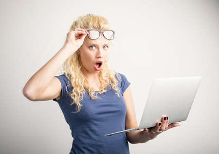 Woman in disbelief lifting up her glasses and holding laptopの写真素材