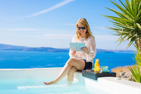 Woman using tablet while sitting by the poolの写真素材