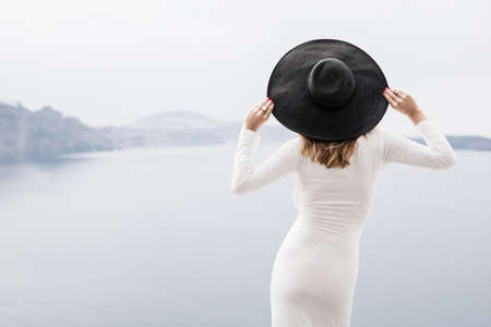 Stylish woman in white dress and black hat from behindの写真素材