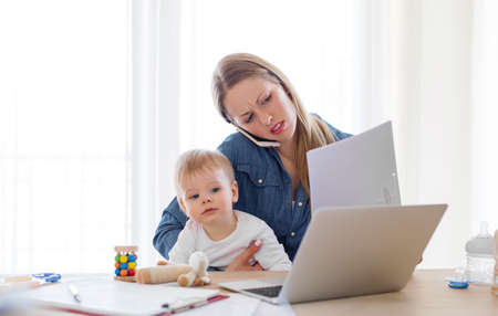 Mother with child in her lap working on computer from homeの写真素材