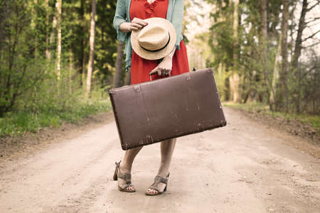 Woman in dress and vintage suitcase standing in the middle of the roadの写真素材