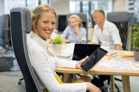 Woman in office holding tablet with co-workers in backgroundの写真素材